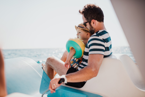 A father with small son sitting on boat on summer holiday.