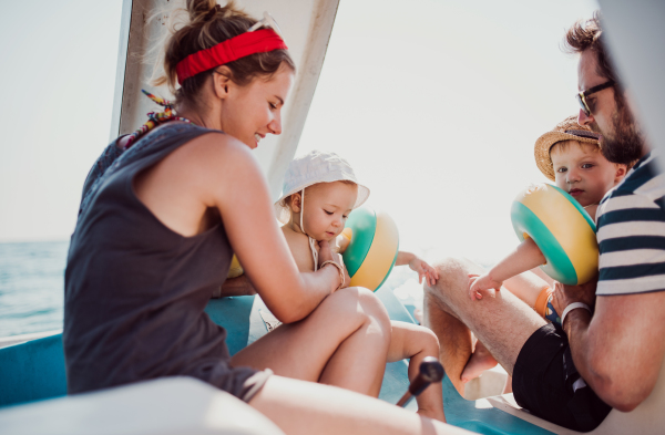 Happy parents with two small toddler children sitting on boat on summer holiday.