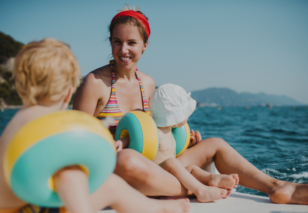 A mother and two small toddler children with armbands sitting on beach on summer holiday.