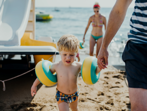 A family with two small toddler children walking on beach on summer holiday.