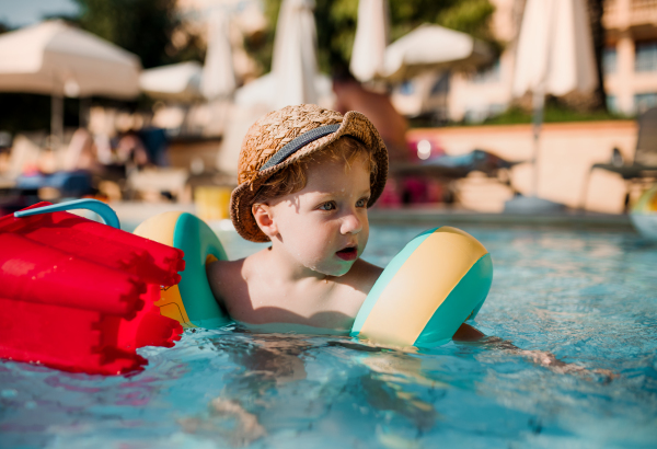 A happy small toddler boy with armbands swimming in water on summer holiday.