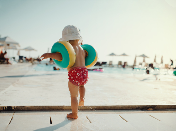 A rear view of small child with armbands walking on beach on summer holiday.