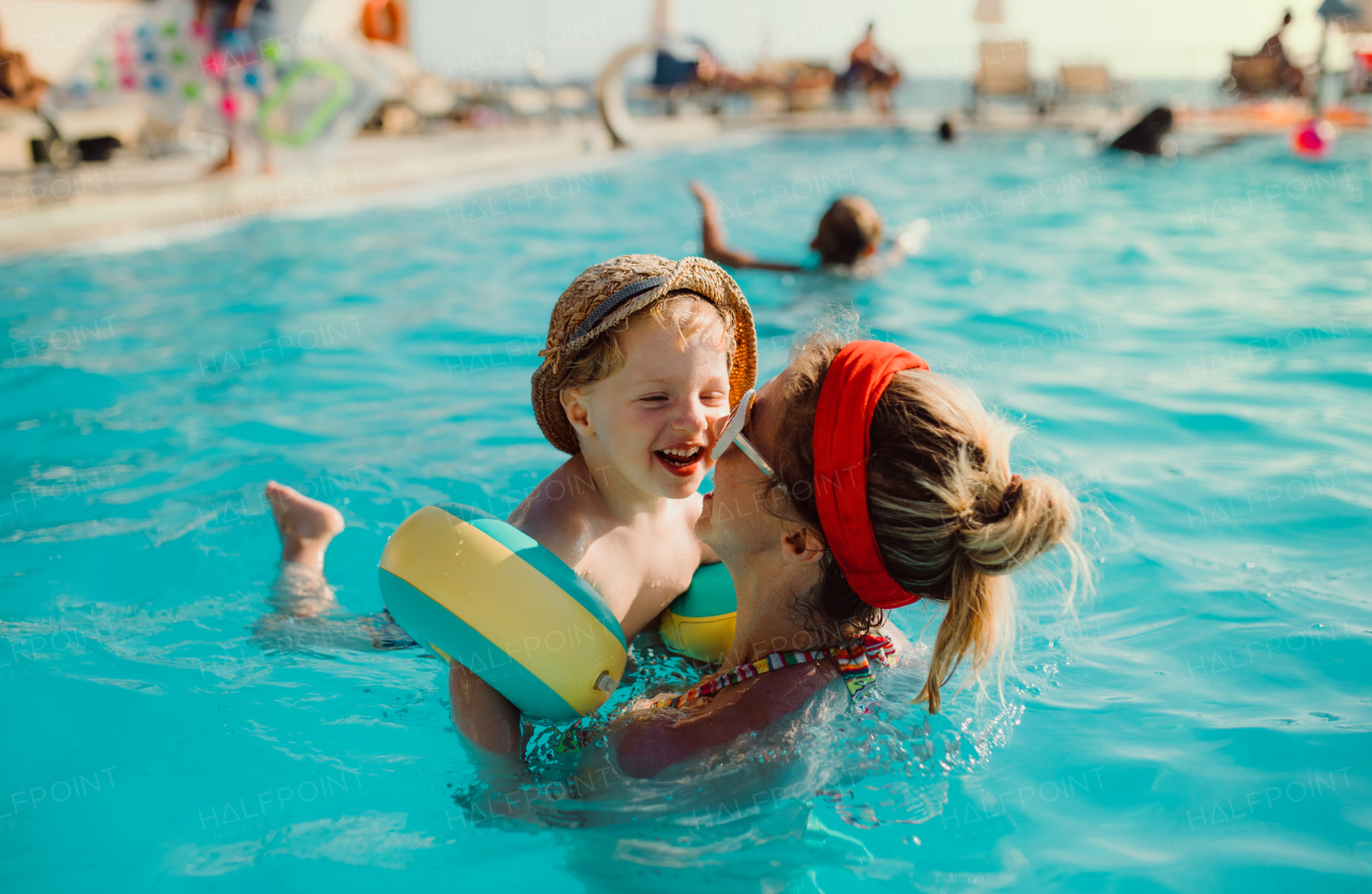 A happy small toddler boy with armbands and his mother swimming in water on summer holiday.