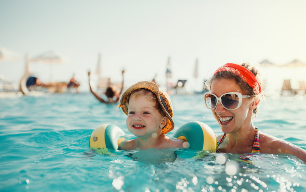 A happy small toddler boy with armbands and his mother swimming in water on summer holiday.