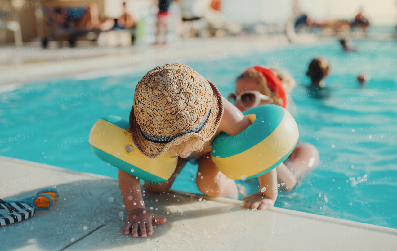 A happy small toddler boy with armbands and his mother swimming in water on summer holiday.