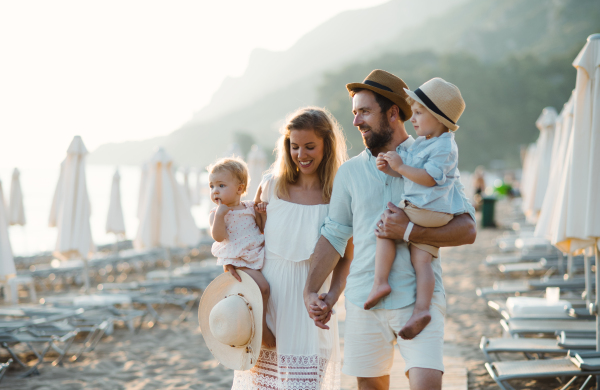 A young family with two toddler children walking on beach on summer holiday, holding hands.