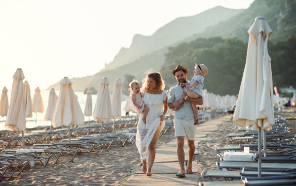 A young family with two toddler children walking on beach on summer holiday.