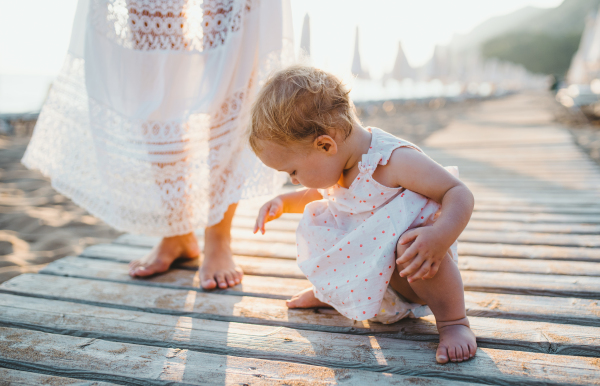 A midsection of young mother with a toddler girl on beach on summer holiday.