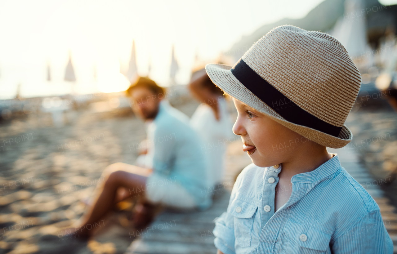 A small toddler boy with a hat standing on beach on summer holiday. Copy space.