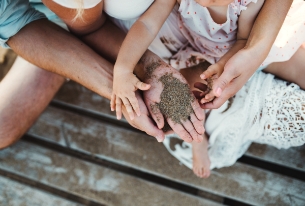 A midsection of family with a toddler girl sitting on sand beach on summer holiday. A close-up and top view.