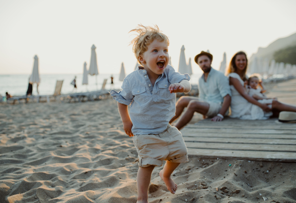 A young family with toddler children having fun on beach on summer holiday.