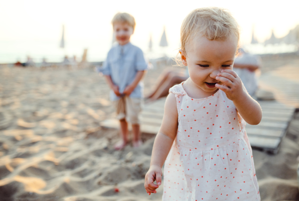 A young family with toddler children having fun on beach on summer holiday.