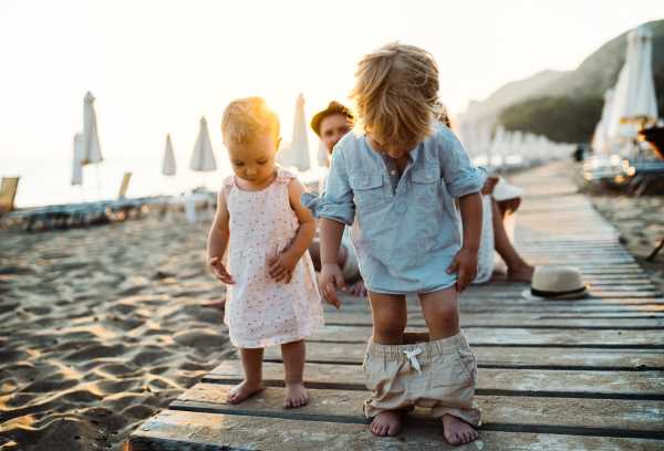 A young family with toddler children having fun on beach on summer holiday.