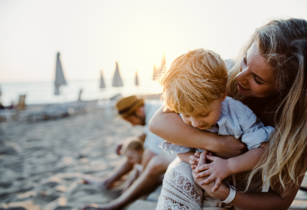 A young family with toddler children having fun on beach on summer holiday.