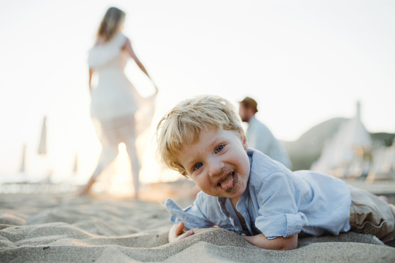 A cheerful small toddler boy standing on beach on summer holiday, having fun.