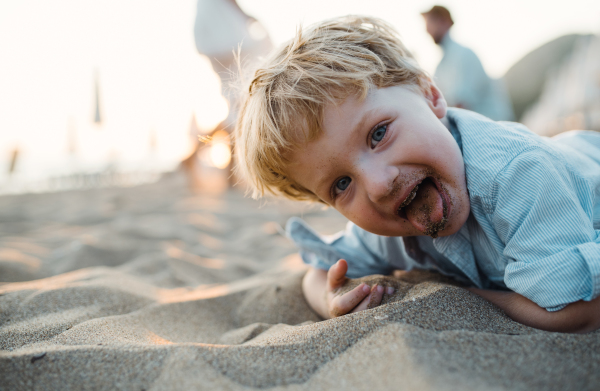 A cheerful small toddler boy standing on beach on summer holiday, having fun.