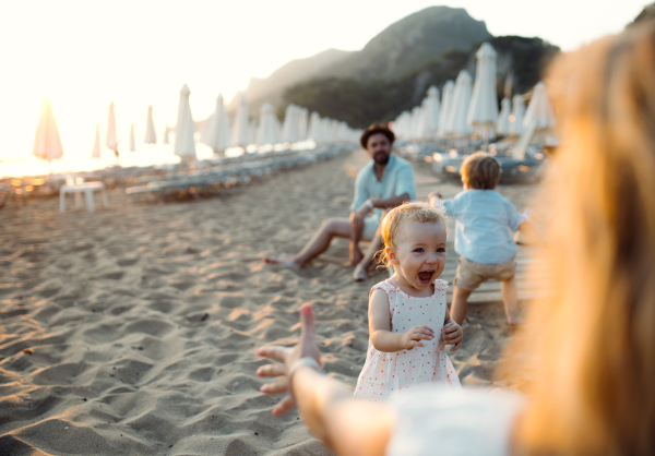 A young family with toddler children having fun on beach on summer holiday. Copy space.