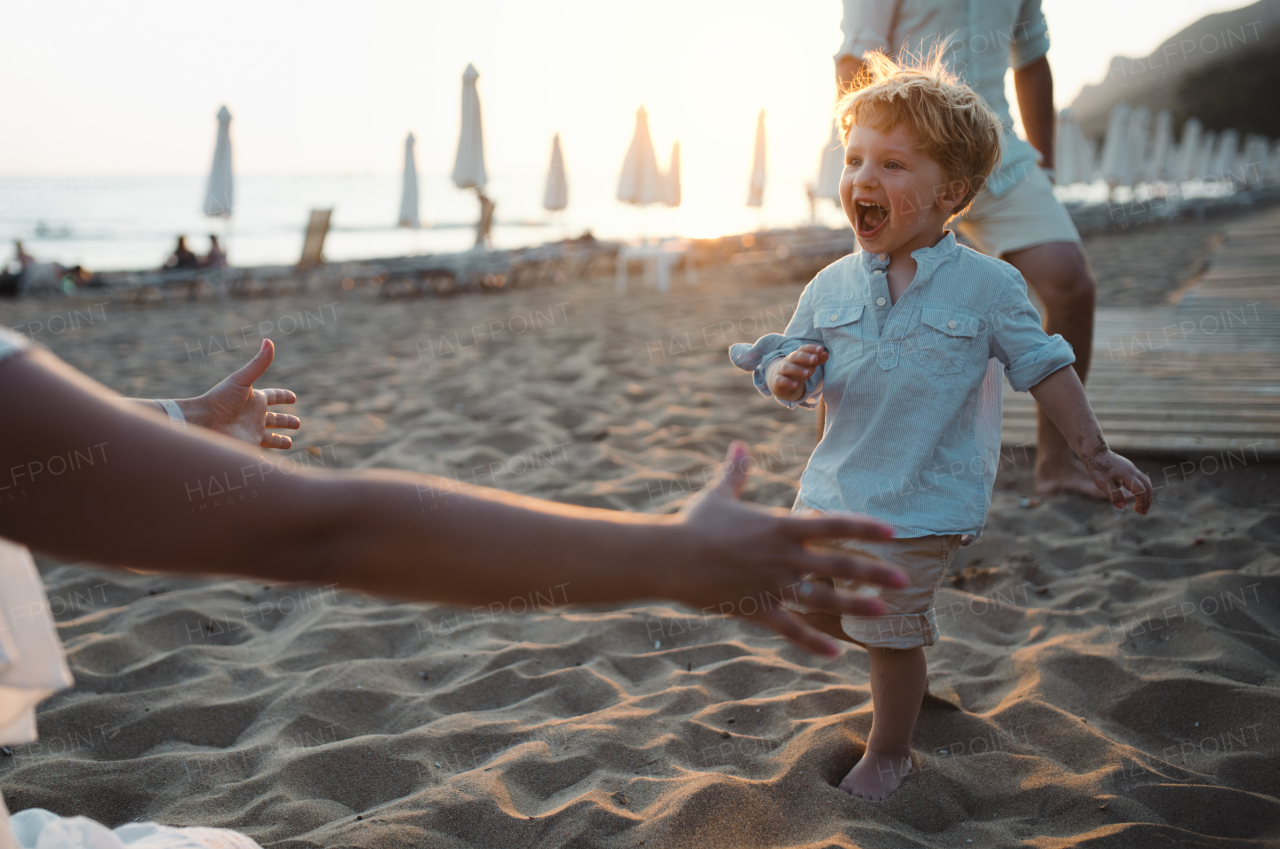 A young family with toddler boy having fun on beach on summer holiday.