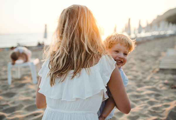 A young mother with a toddler boy having fun on beach on summer holiday.