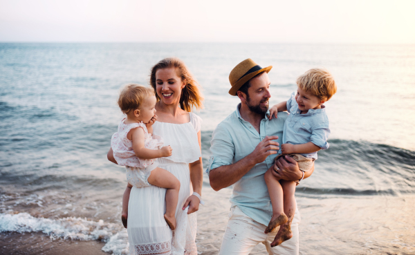 A young family with two toddler children walking on beach on summer holiday.