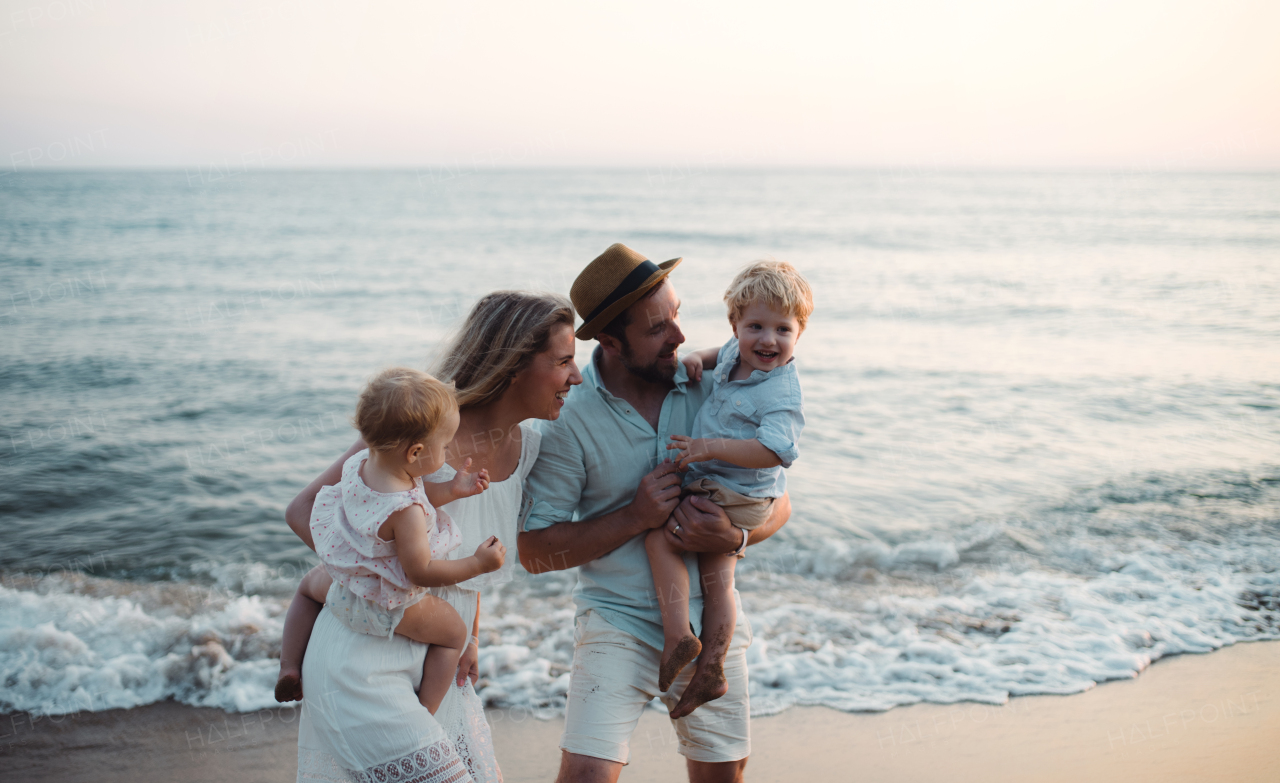 A young family with two toddler children standing on beach on summer holiday, laughing.