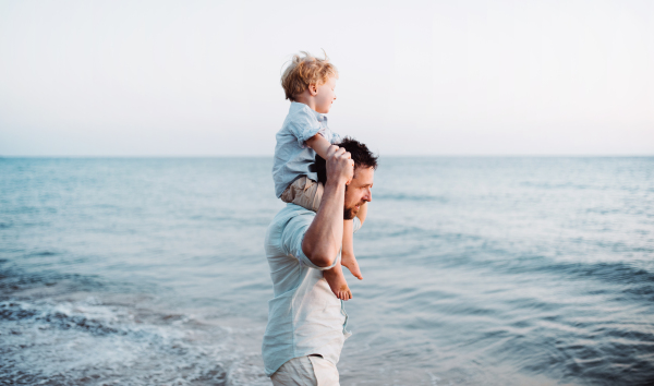 Mature father with a toddler boy walking on beach on summer holiday, having fun.