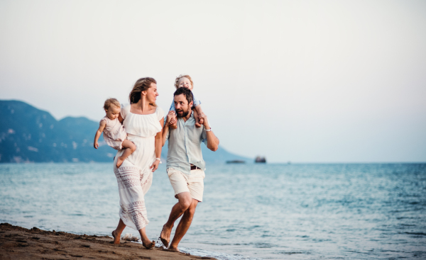 A young family with two toddler children walking on beach on summer holiday.