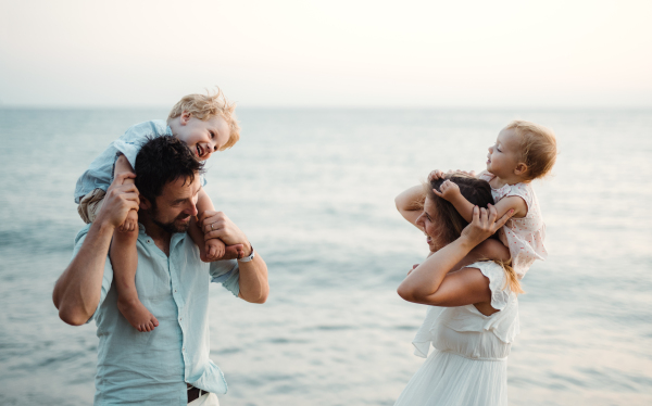 A young family with two toddler children standing on beach on summer holiday, laughing.