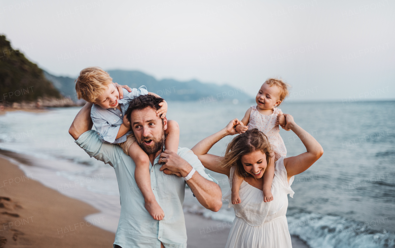 A young family with two toddler children standing on beach on summer holiday, laughing.