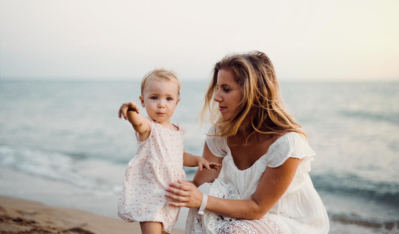 A young mother with a toddler girl on beach on summer holiday.