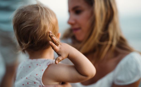 A close-up of young mother with a toddler girl on beach on summer holiday.