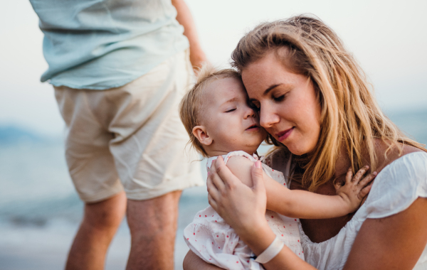 A close-up of young mother with a toddler girl on beach on summer holiday.