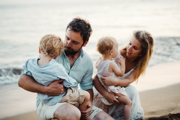 A family with two toddler children sitting on sand beach on summer holiday, playing.