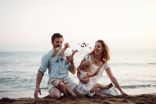 A family with two toddler children sitting on sand beach on summer holiday, playing.