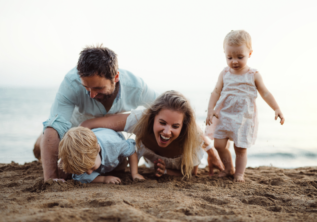 A young family with toddler children playing with sand on beach on summer holiday.