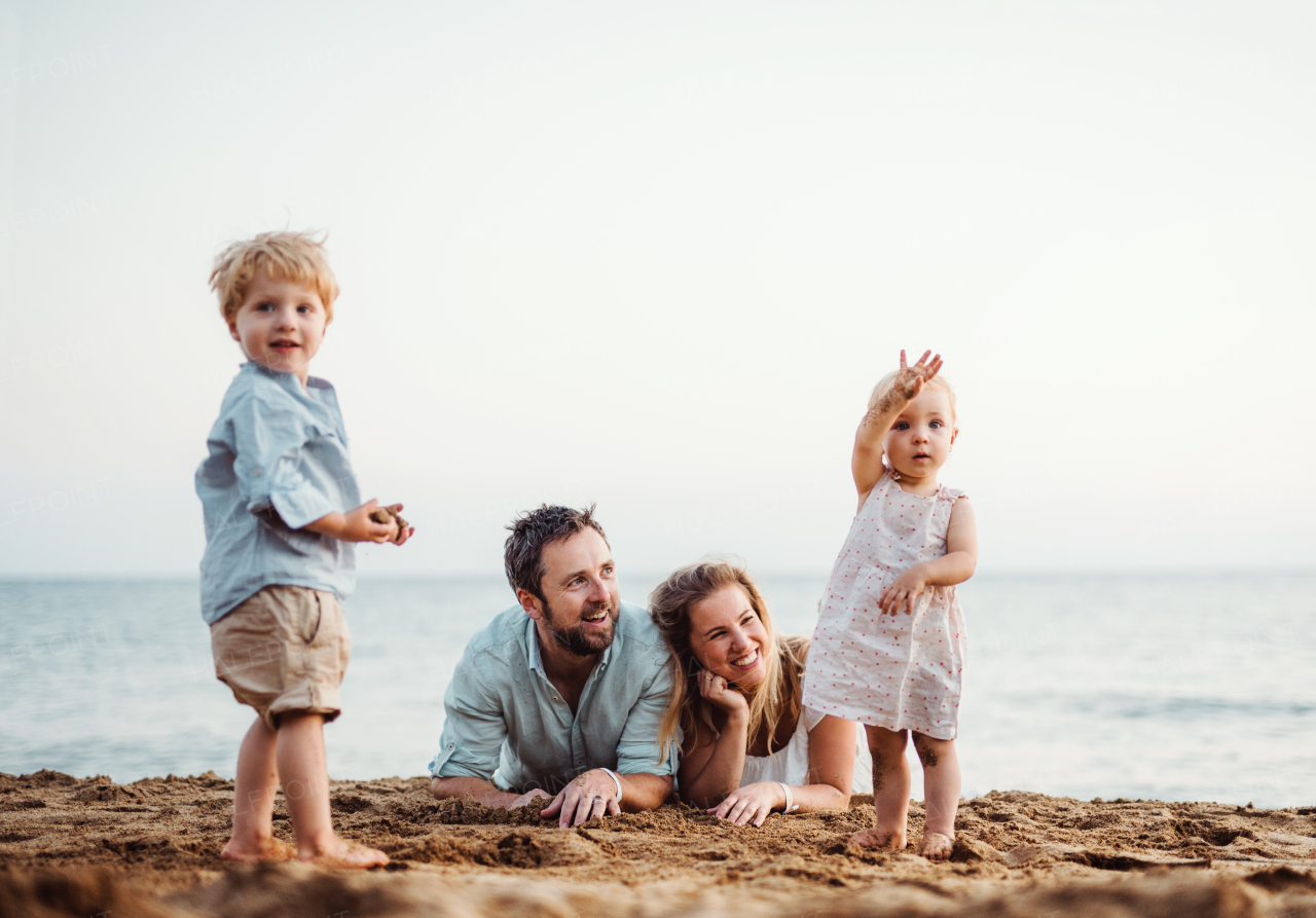 A family with two toddler children lying on sand beach on summer holiday, playing.