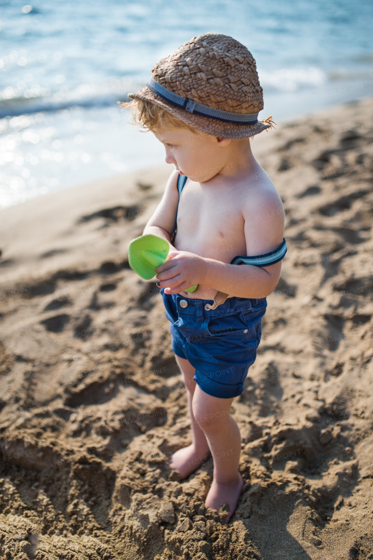 An occupied small toddler boy sitting on beach on summer holiday, playing.