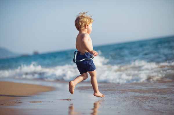 A cute small toddler boy with shorts running on sand beach on summer holiday. Copy space.