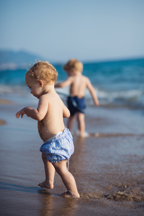 Two shirtless toddler children walking on a beach on summer holiday.