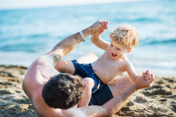 A father with a happy toddler son playing on sand beach on summer holiday.