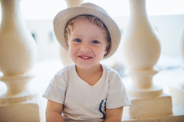 A front view of small toddler boy sitting in front of concrete railing or balustrade on summer holiday.