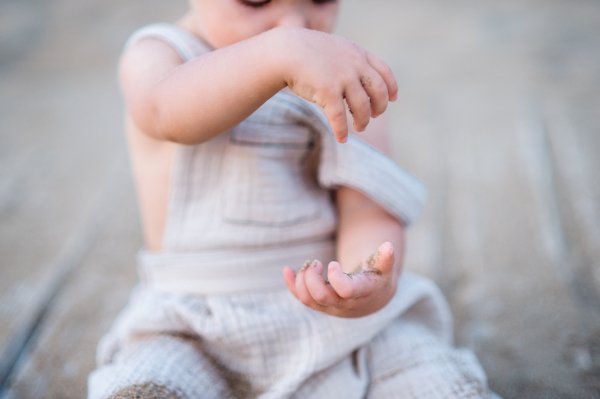 A midsection of unrecognizable small toddler girl sitting on beach on summer holiday, playing.