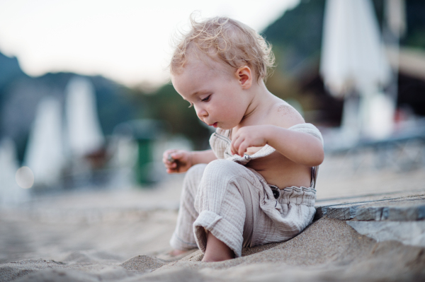 A cute small toddler girl sitting on beach on summer holiday. Copy space.