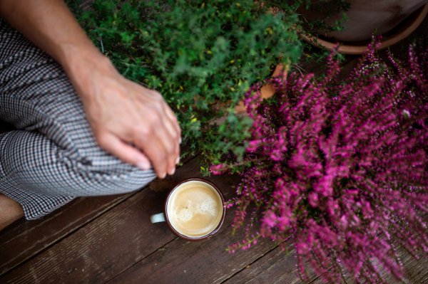 A midsection of woman with coffee sitting outdoors on terrace, resting.