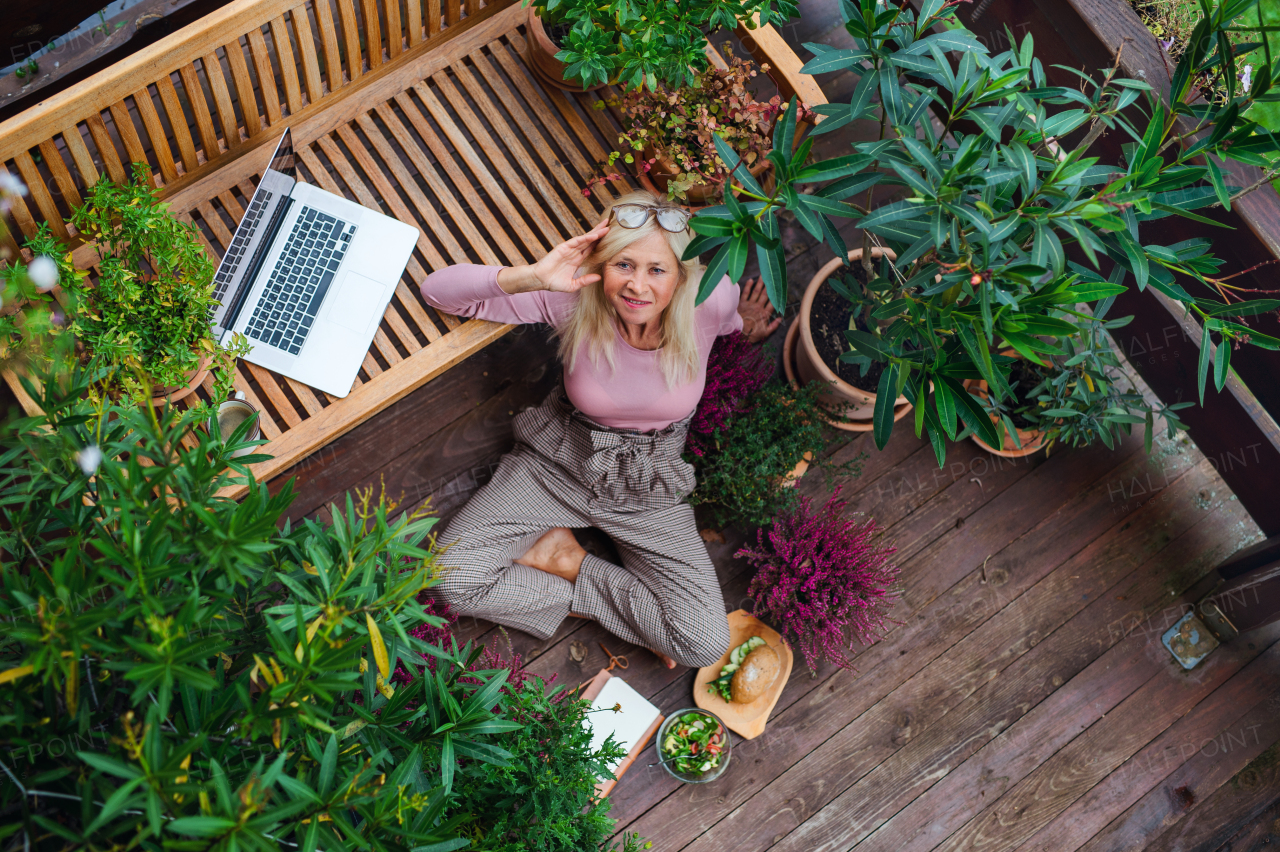 Top view of senior woman with laptop conmputer sitting outdoors on terrace, resting.