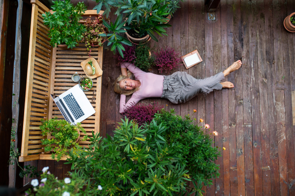 A top view of senior woman with laptop lying outdoors on terrace, resting.