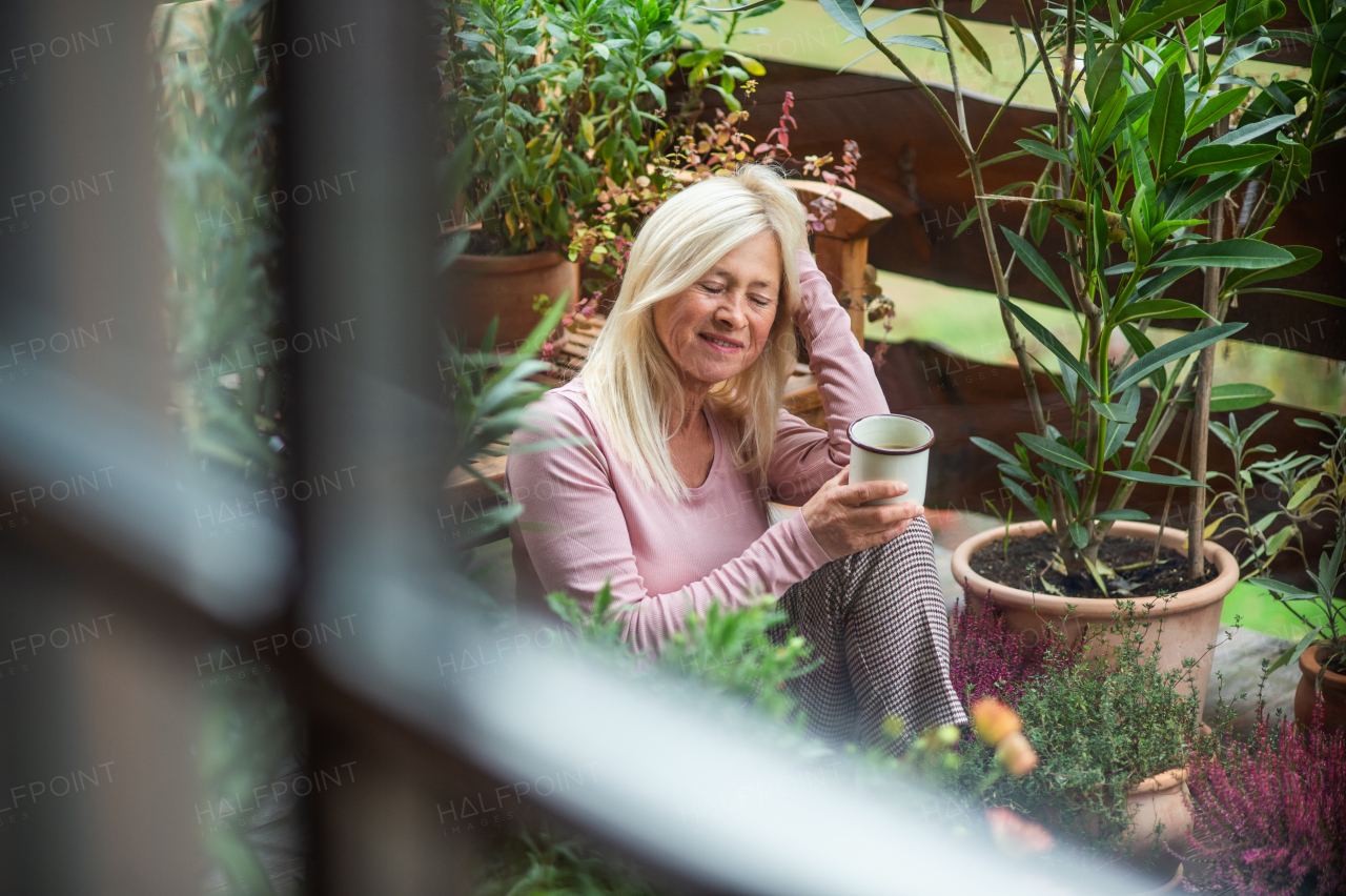 Senior woman with cup of coffee sitting outdoors on terrace, resting.