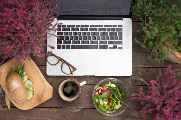 A composition of laptop and lunch on bench outdoors on terrace.