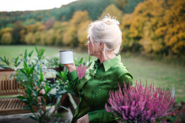 A senior woman with coffee standing outdoors on terrace, resting.