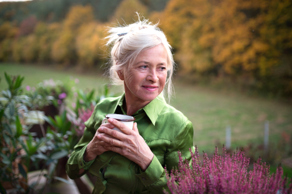 A senior woman with coffee standing outdoors on terrace, resting.